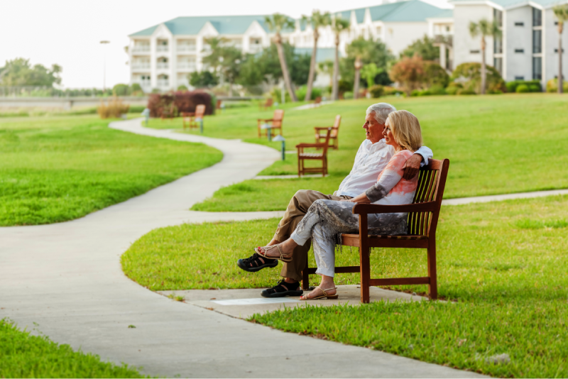 Elderly, retired couple sitting on a bench outside a retirement community on a sunny day in Florida