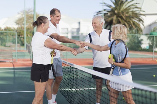 Senior couple shaking hands with another couple on a tennis court
