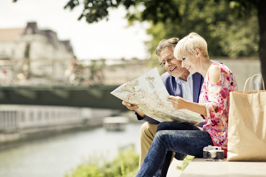 Seniors looking at a map, sitting on a bench while traveling