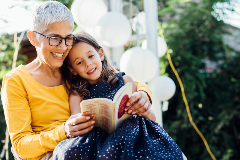 Senior woman with her grandaughter sitting on her lap reading a book together