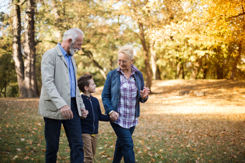 Grandparents holding hands with their grandson as they walk through a park during the Fall