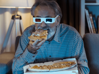 Senior man eating slice of pizza holding pizza box and wearing 3D glasses