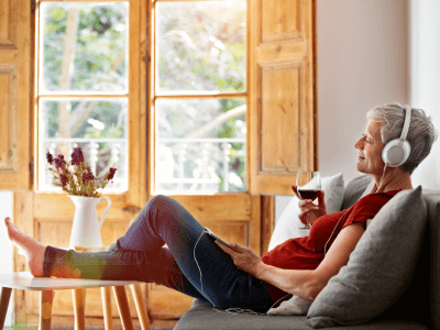 Mature woman sitting on her sofa listening to music on a digital tablet and drinking wine
