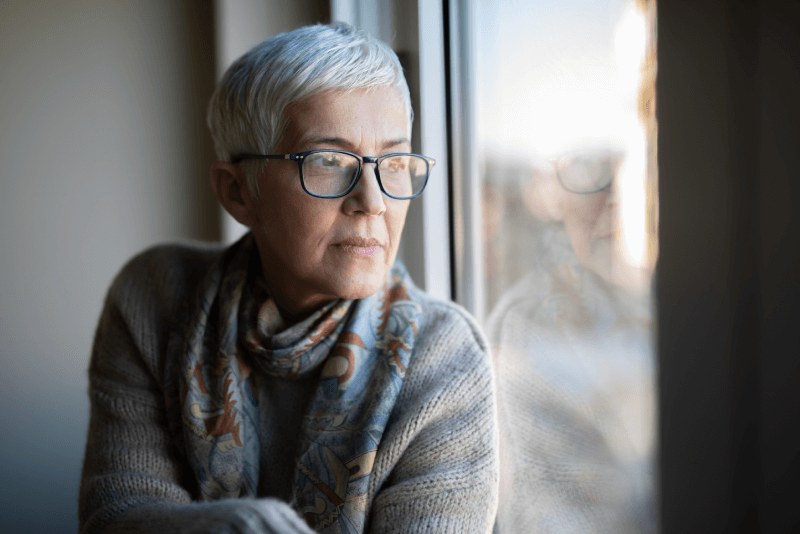 Senior woman looking out her house window practicing shelter in place
