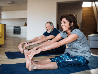 A senior couple indoors at home, doing exercise on the floor.