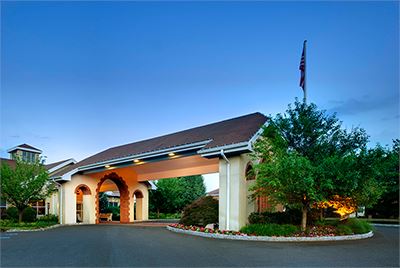 Single-story building with a covered entryway, surrounded by landscaping and trees, under a clear blue sky at dusk.