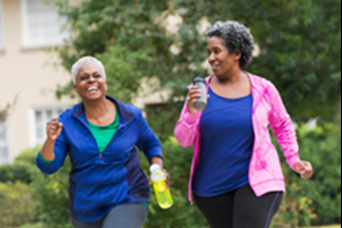 Two women in athletic wear walk outdoors, smiling. One holds a water bottle. Trees and a building are visible in the background.