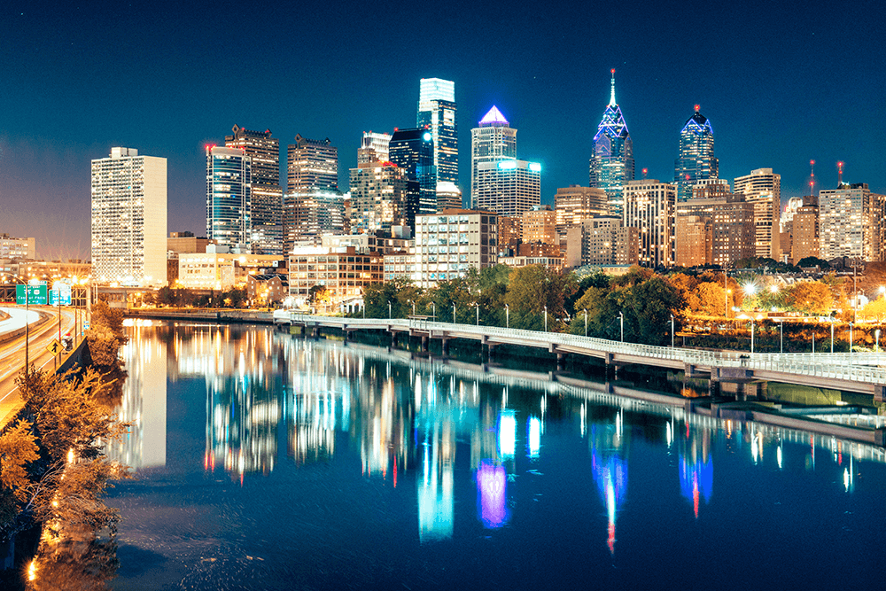 Philadelphia city skyline at night with illuminated buildings reflecting on the Schuylkill River.