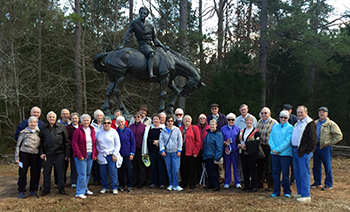 A group of adults poses in front of a statue of a person on horseback, surrounded by trees.