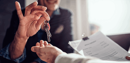 A person hands over a set of keys to another person, who is also holding paperwork clipped together.