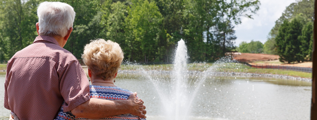 Retired couple in the sun looking at a pond with a fountain