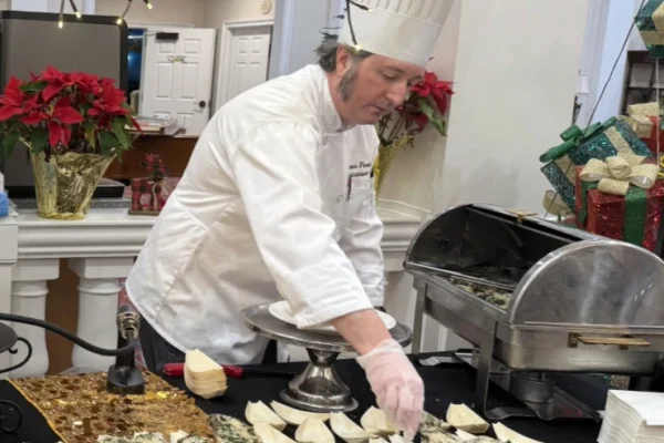 A chef in a white uniform and tall hat arranges hors d’oeuvres on a buffet table.